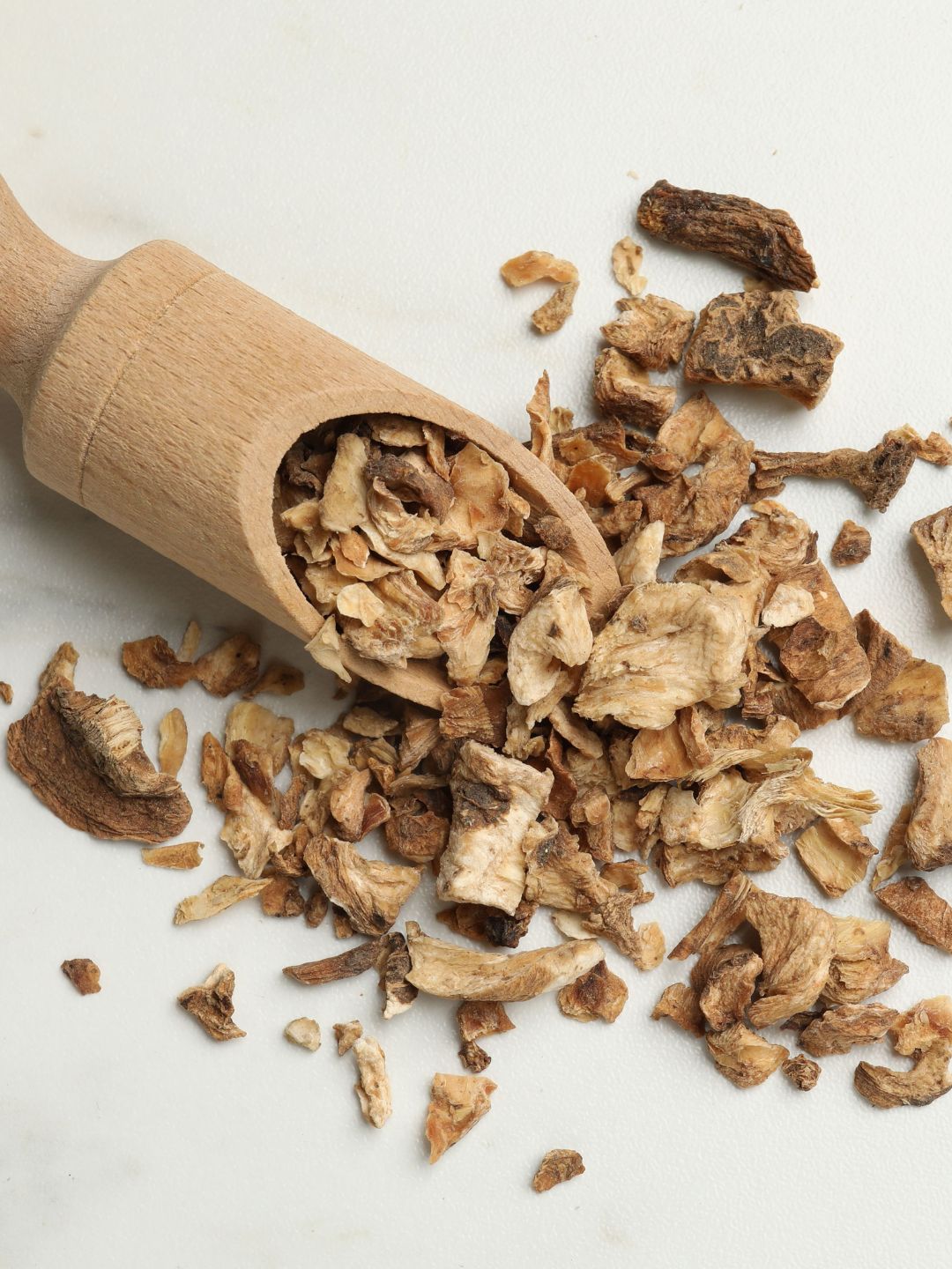 A wooden scoop spilling pieces of dried chicory root onto a pale background, the source of Hydrosil's prebiotic