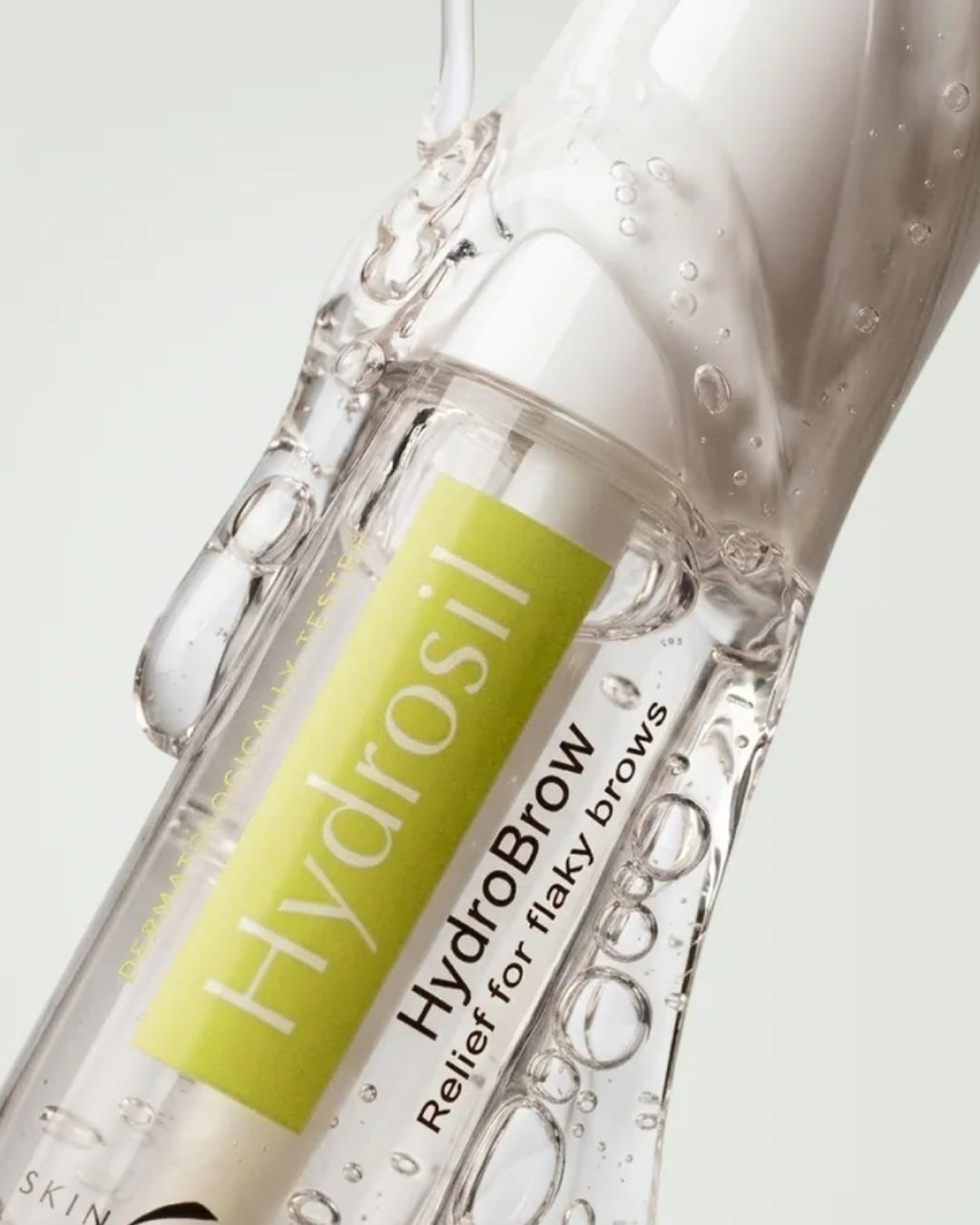 Close-up of the Hydrosil Hydrobrow Serum bottle surrounded by clear gel and bubbles, showing the light, clear texture and green Hydrosil label