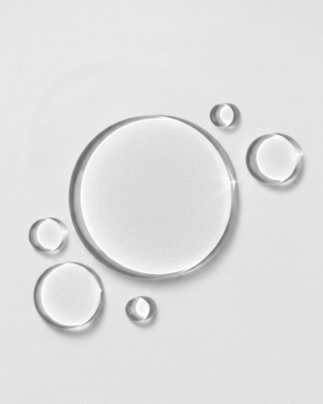 Clear droplets of Hydrosil Scalp Shield Shampoo on a pale grey background, showing its light, gel-like texture