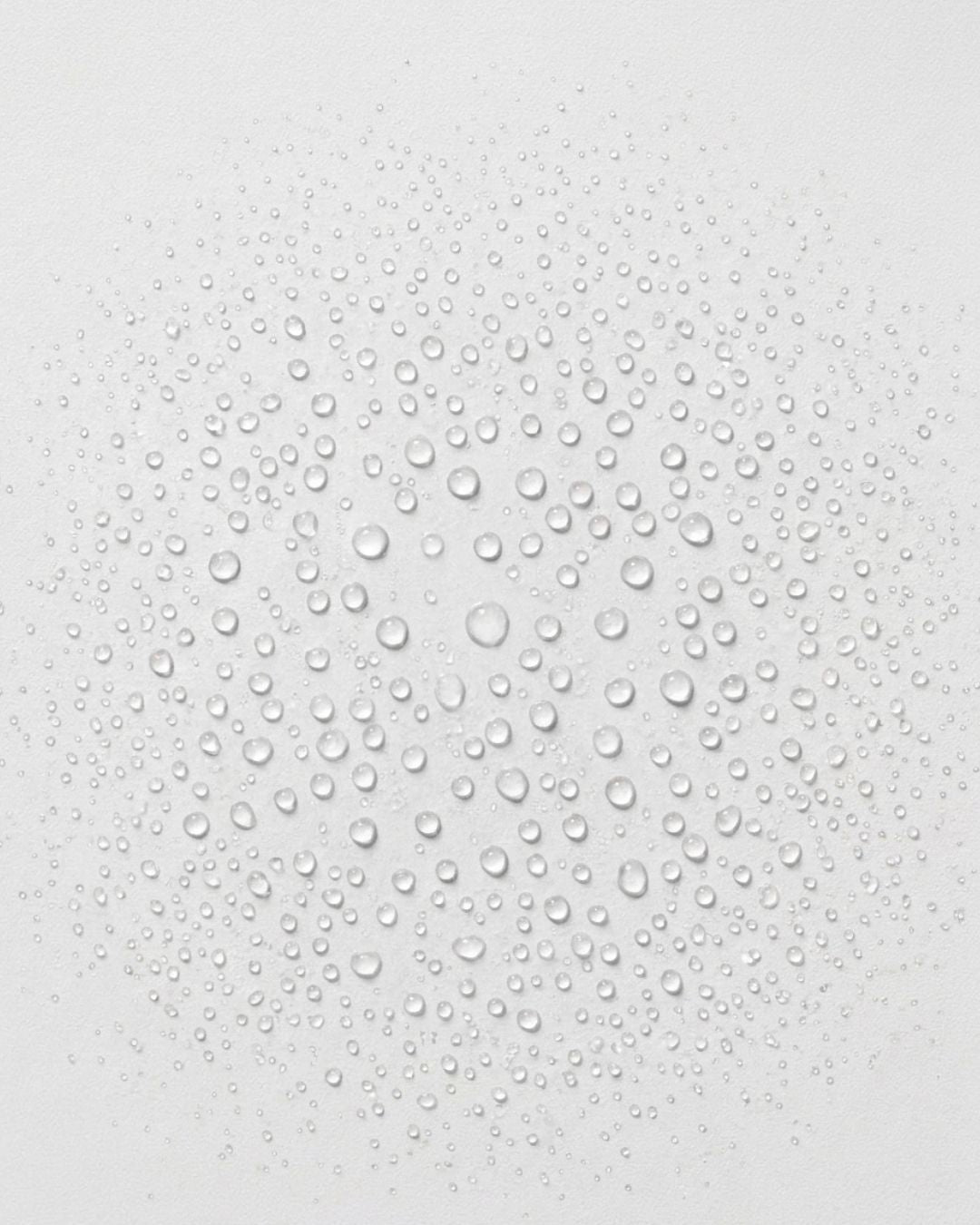 Fine droplets of clear liquid scattered across a soft white surface, evoking the fine mist and hydration of Hydrosil Scalp Shield Tonic spray.