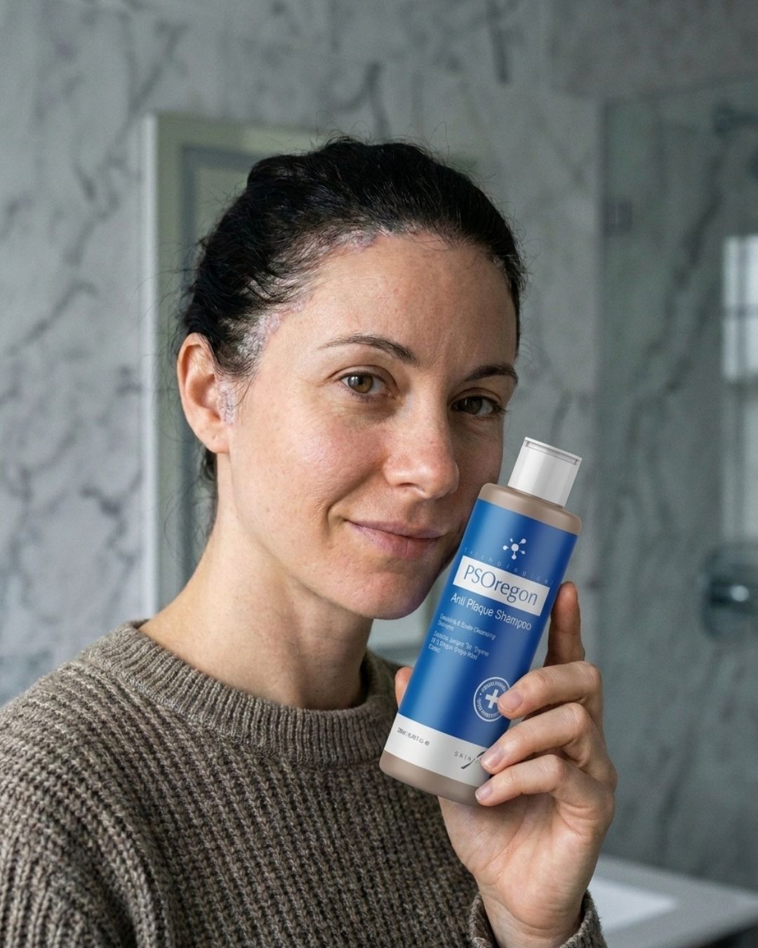 Woman holding PSOregon Anti-Plaque Shampoo to her face, her hairline looking clearer, in a bathroom